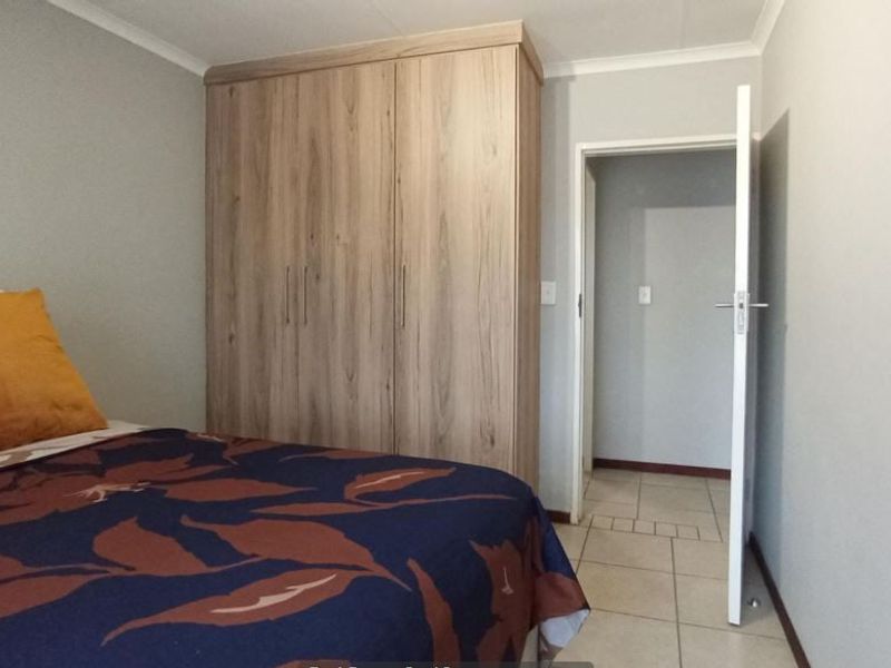 A bedroom featuring light wood-finish built-in wardrobes and neutral tiled flooring, providing a functional and clean living space.
