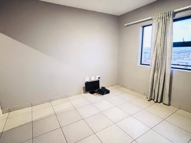 A bright, empty bedroom featuring neutral grey walls, tiled flooring, and a window with curtain track.