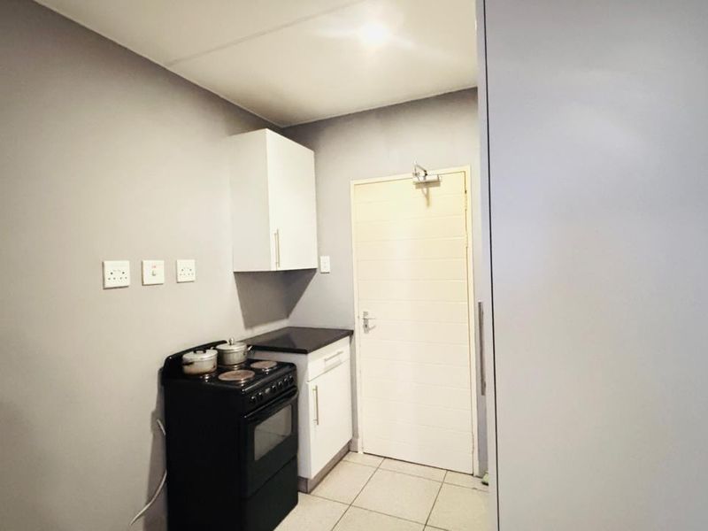 A compact kitchen area featuring a freestanding stove, overhead cabinetry, and tiled flooring, providing essential cooking facilities in a functional layout.