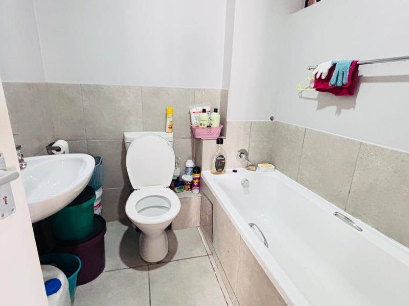 A functional bathroom featuring a standard bathtub, pedestal sink, and toilet with neutral wall and floor tiling.