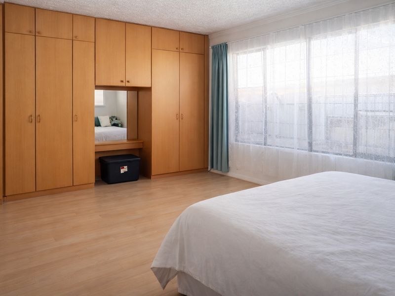 A bedroom featuring extensive light wood built-in cabinetry, laminate flooring, and a large window allowing natural light.
