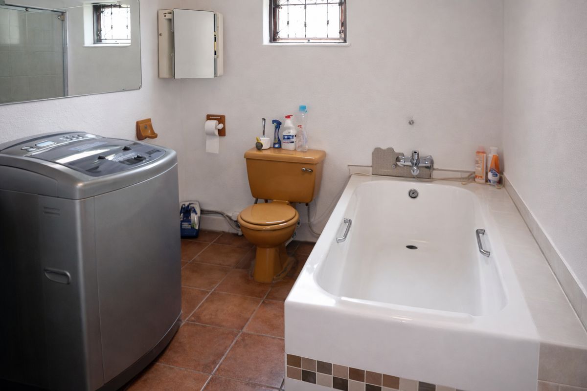 A functional bathroom featuring a bathtub, toilet, and tiled flooring, with a window providing natural light and security bars.