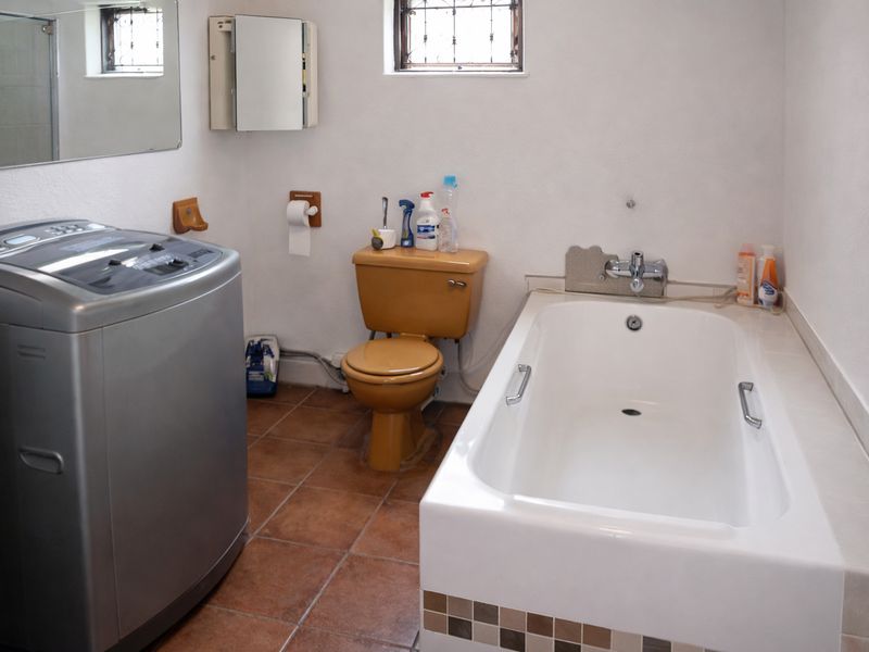 A functional bathroom featuring a bathtub, toilet, and tiled flooring, with a window providing natural light and security bars.