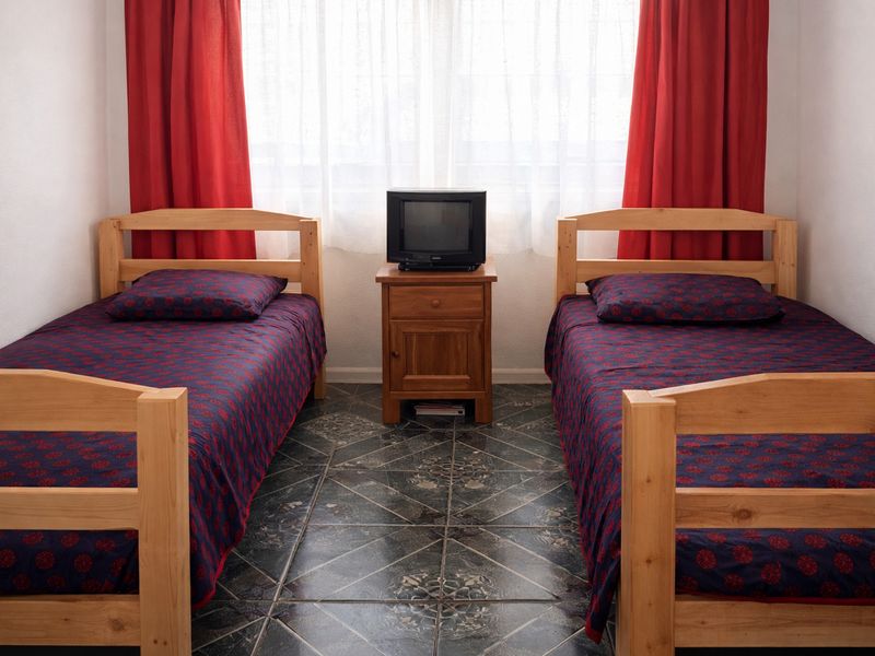 A bedroom featuring tiled flooring and a window with curtains, currently configured with two single beds.