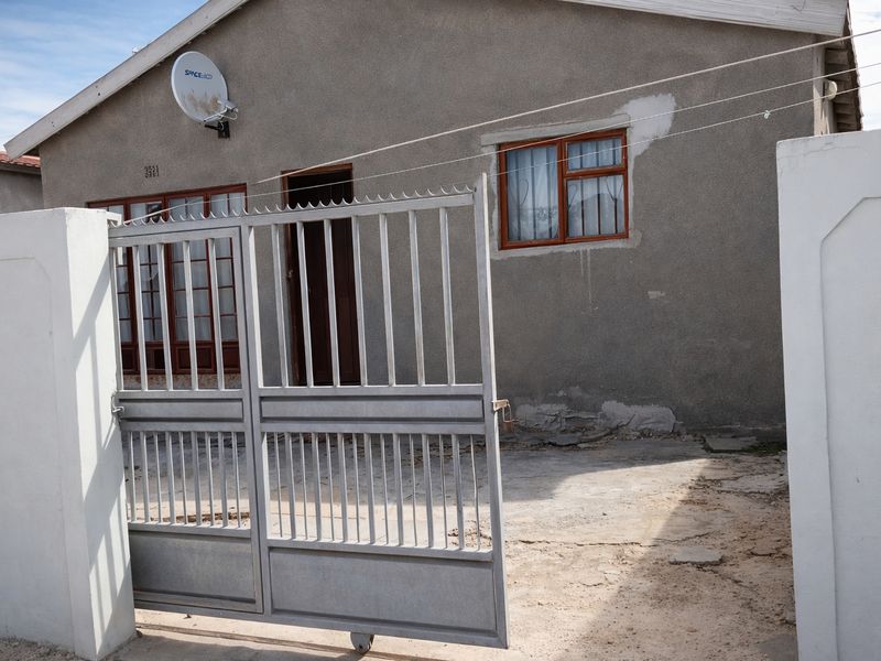 Front exterior view of the property featuring a metal security gate, concrete driveway, and plastered facade with window security bars.