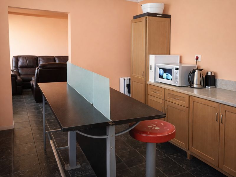 A functional kitchen area featuring built-in wooden cabinetry, laminate countertops, and tiled flooring, with an adjacent living space visible through the doorway.