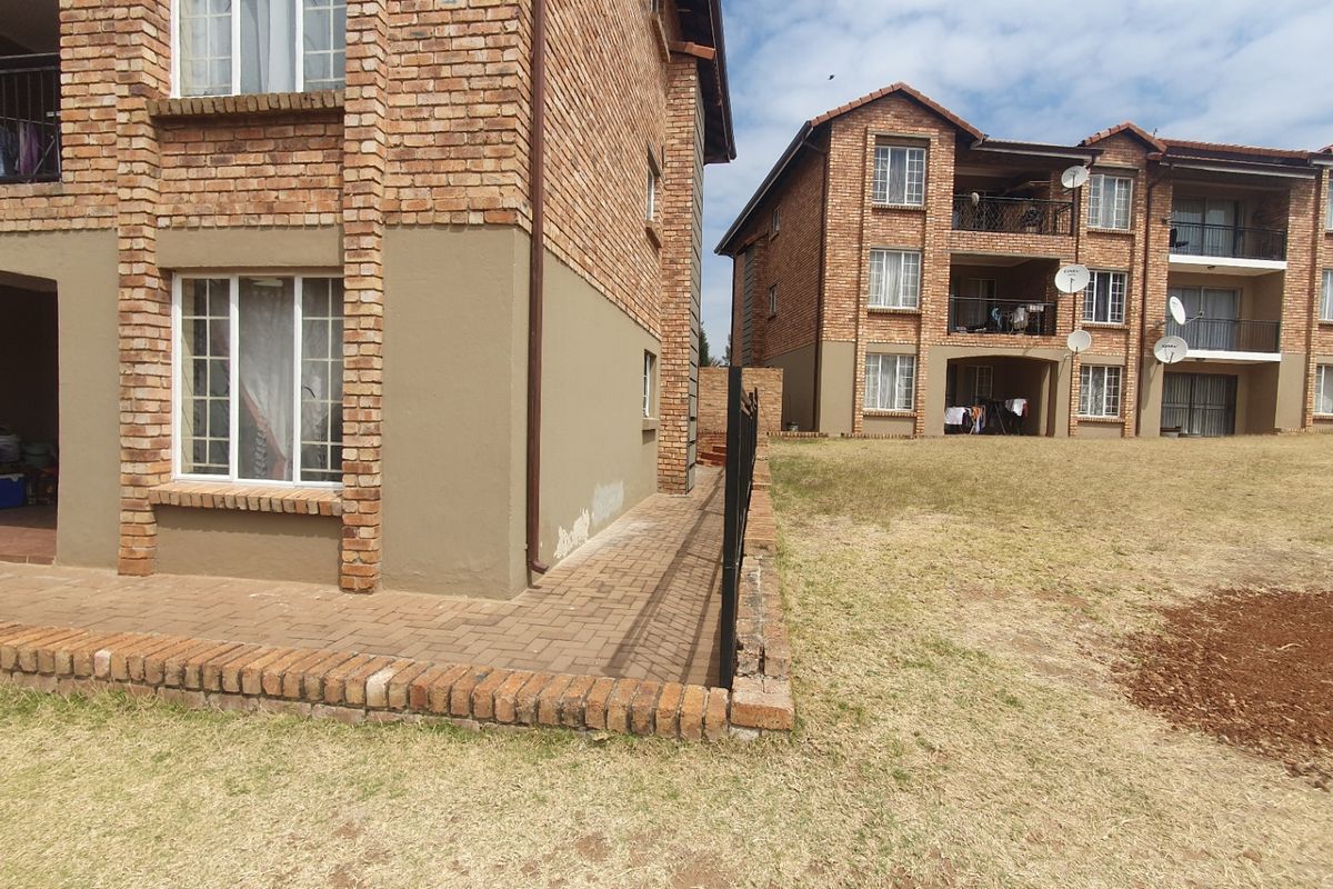 Exterior view of a multi-story brick apartment complex featuring paved patio areas and communal lawn space.
