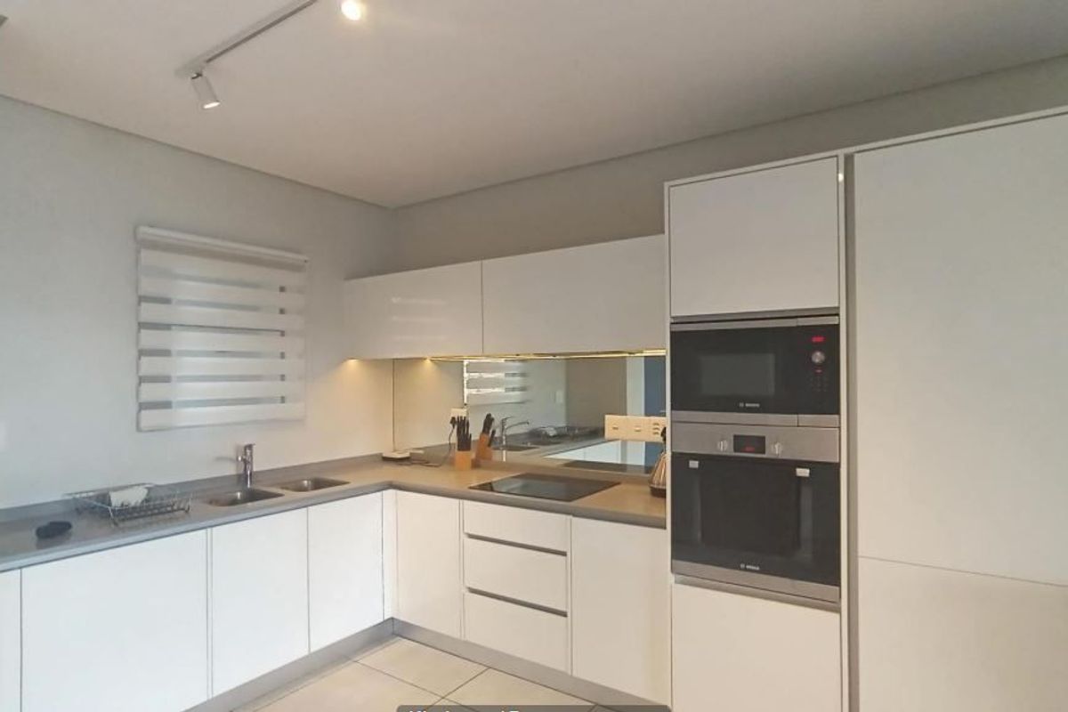 Modern kitchen featuring sleek white cabinetry, integrated appliances, induction hob, mirror splashback, and neutral tiled flooring.