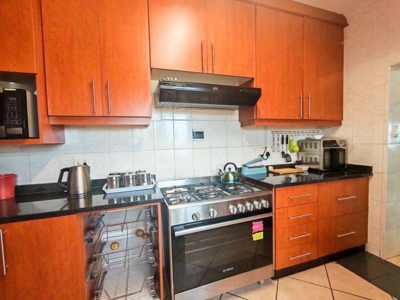 A functional kitchen featuring warm-toned wooden cabinetry, granite countertops, a gas stove with extractor fan, and a tiled backsplash.