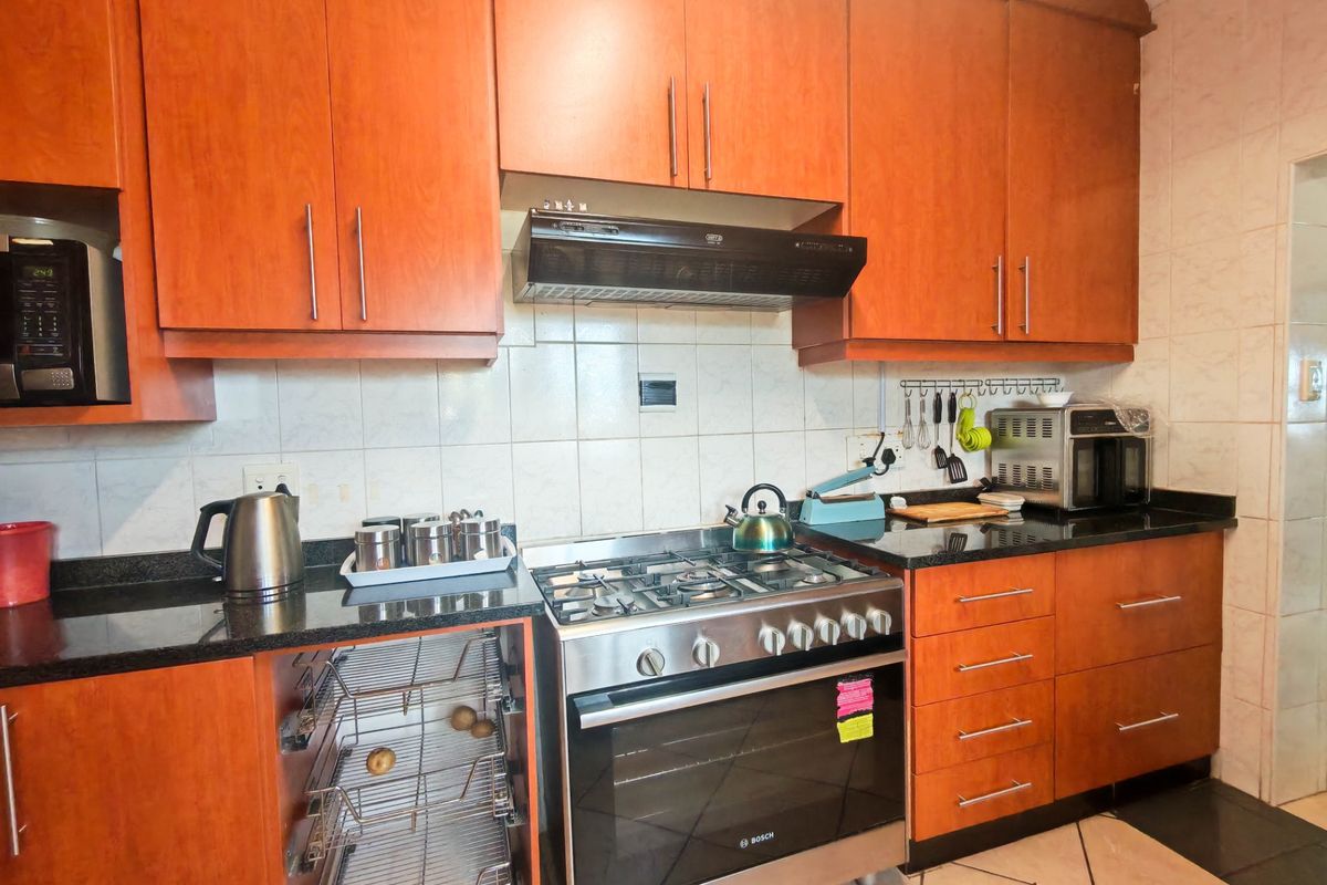 A functional kitchen featuring warm-toned wooden cabinetry, granite countertops, a gas stove with extractor fan, and a tiled backsplash.