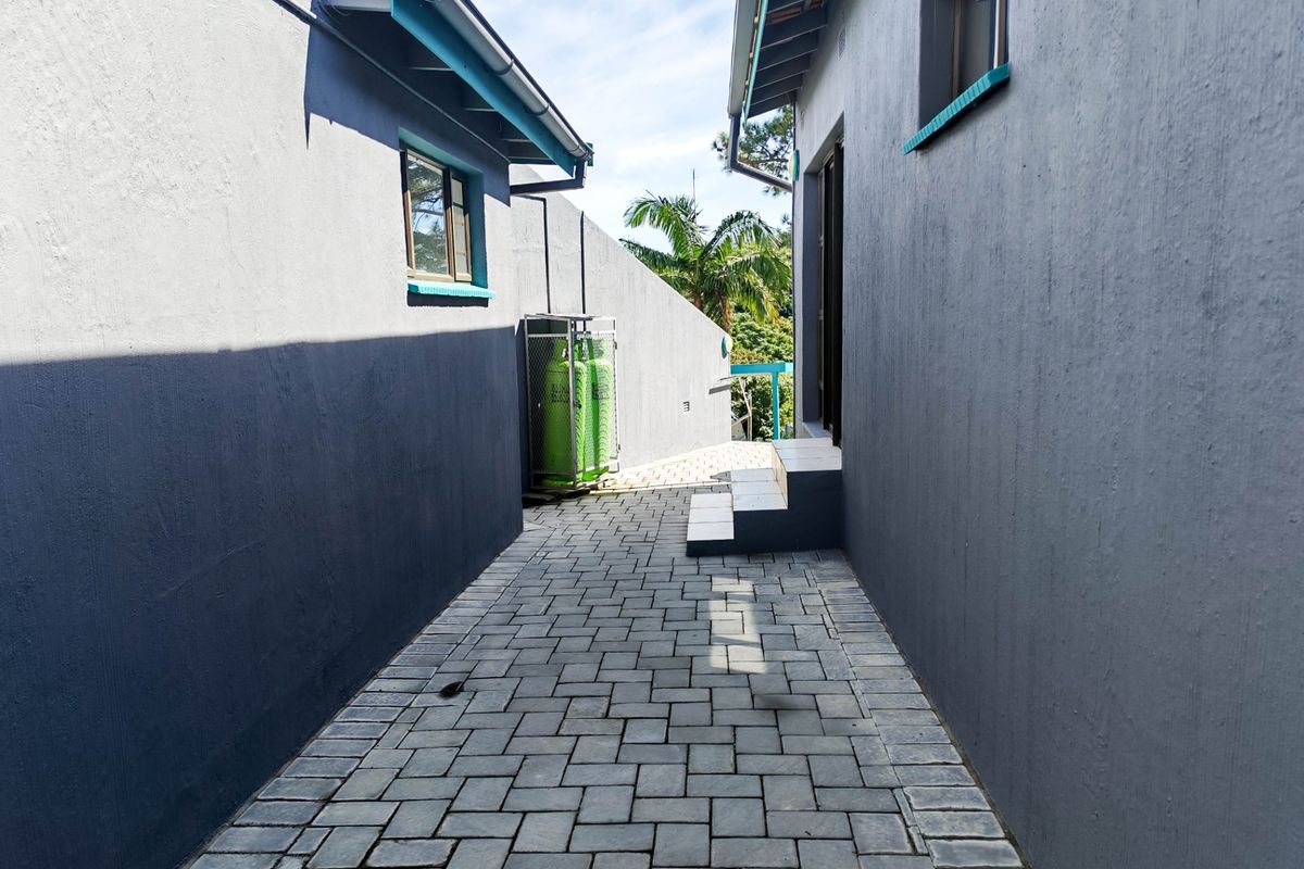 A paved side walkway between two sections of the house, featuring a secure gas cylinder storage cage and external steps.