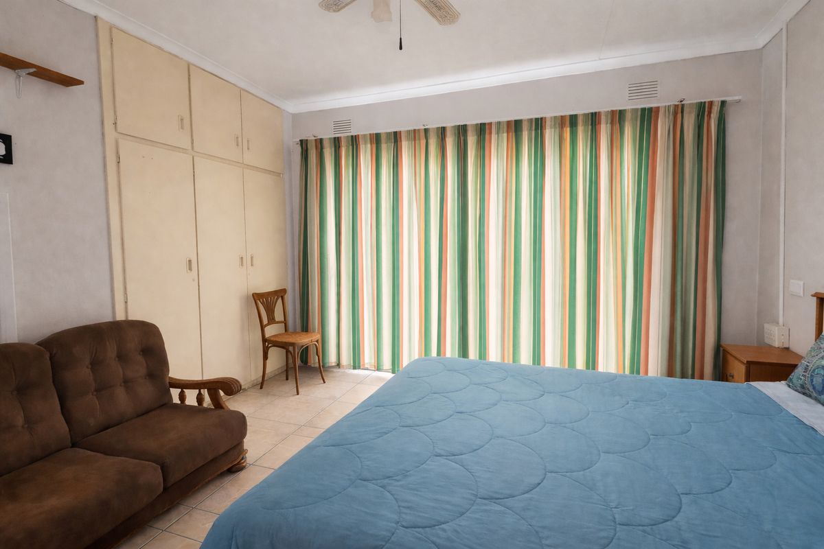 A spacious bedroom featuring built-in cupboards, tiled flooring, and a ceiling fan, offering a functional layout with potential for modern updates.