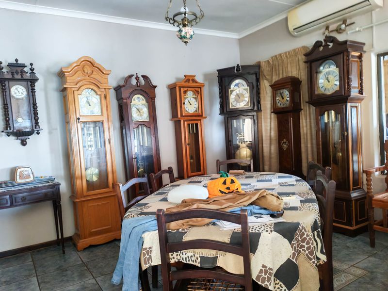 A dining room featuring tiled flooring and a wall-mounted split-system air conditioner, currently utilized as a display area for multiple grandfather clocks.