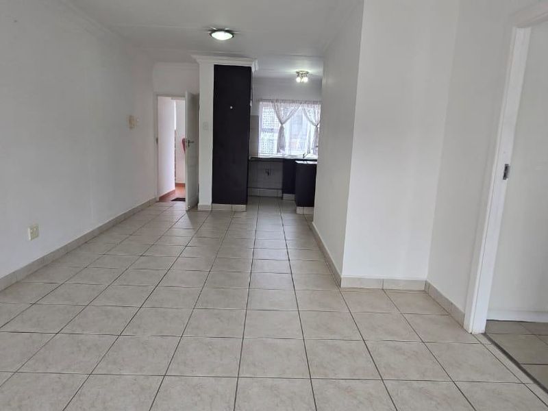 An open-plan living area featuring neutral tiled flooring, built-in storage cupboards, and a view through to the kitchen space.