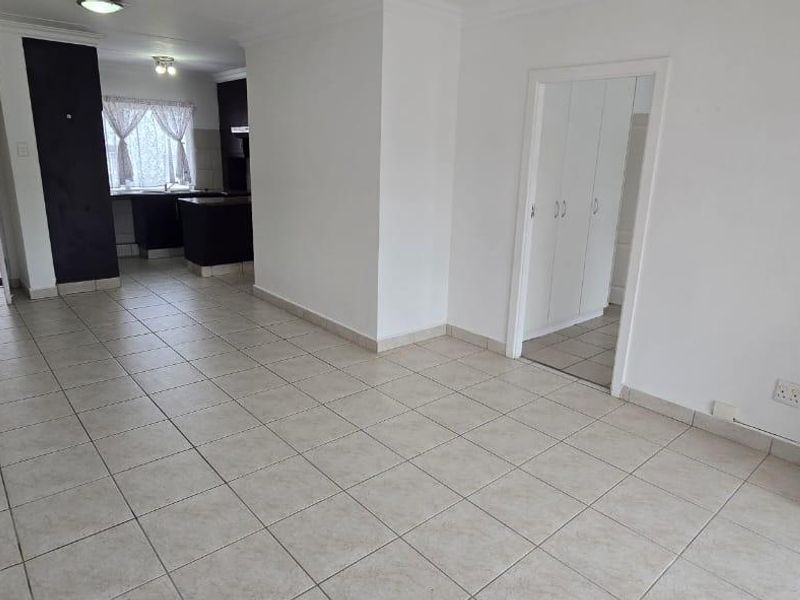 An open-plan living and kitchen area featuring neutral tiled flooring, built-in storage, and clean white walls, offering a versatile space for modern living.