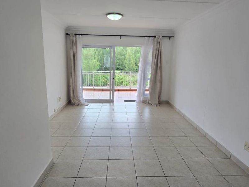 An empty, neutrally finished living room featuring tiled flooring and a sliding glass door that opens onto a balcony.