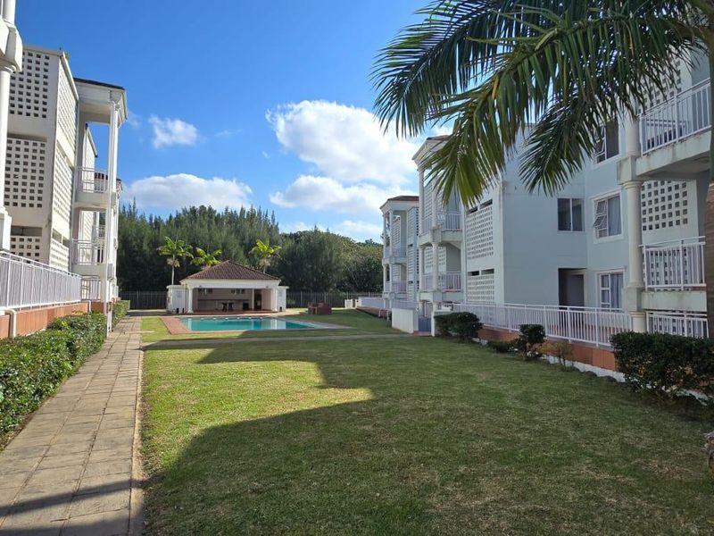 A well-maintained apartment complex exterior featuring a communal swimming pool, landscaped garden, and paved walkways between residential blocks.