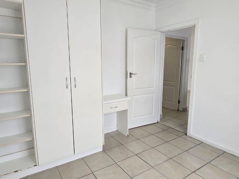 A vacant bedroom featuring neutral tiled flooring, built-in cupboards with integrated shelving, and a small built-in vanity area.