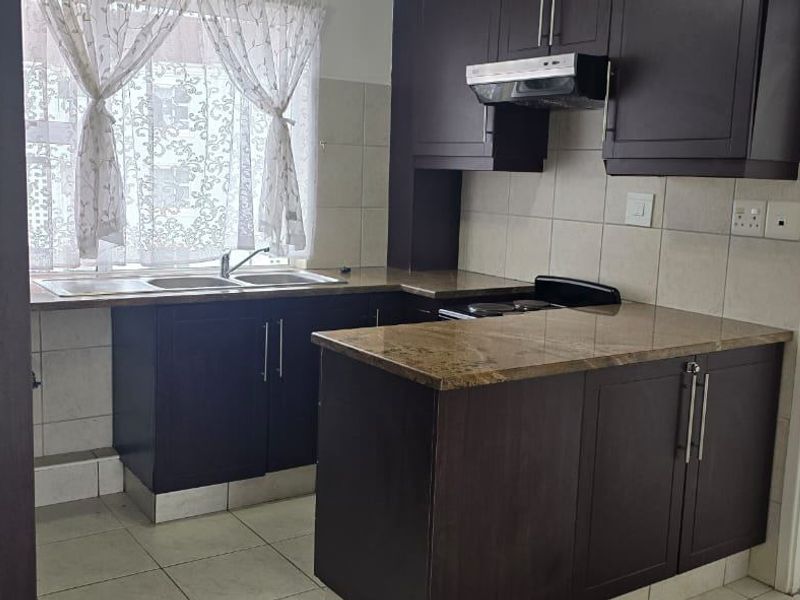 A functional kitchen featuring dark wood cabinetry, granite countertops, a stainless steel double sink, and a built-in extractor fan with tiled finishes.