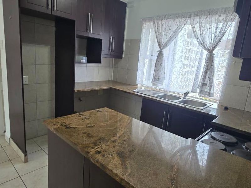 A functional kitchen featuring dark wood cabinetry, granite countertops, a double basin sink, and an integrated electric hob with tiled flooring.
