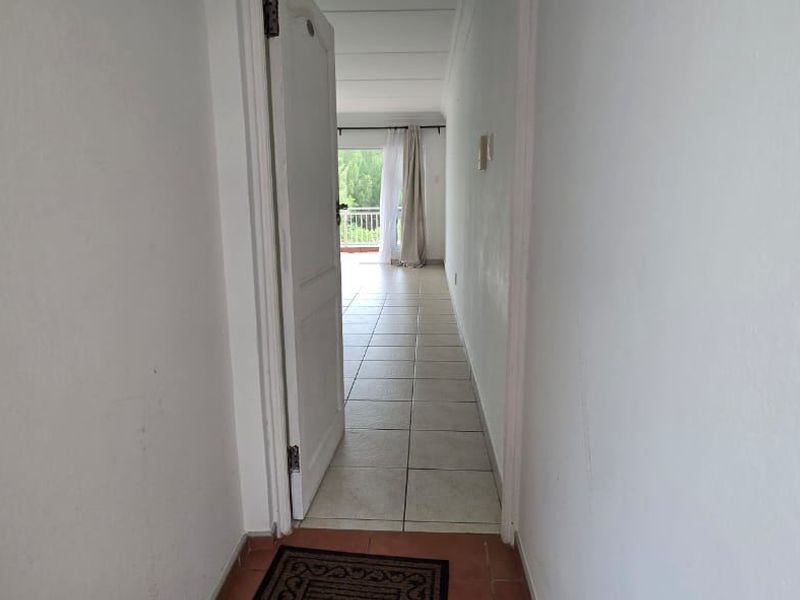 A view through a doorway into a tiled hallway leading towards an open living area with balcony access.