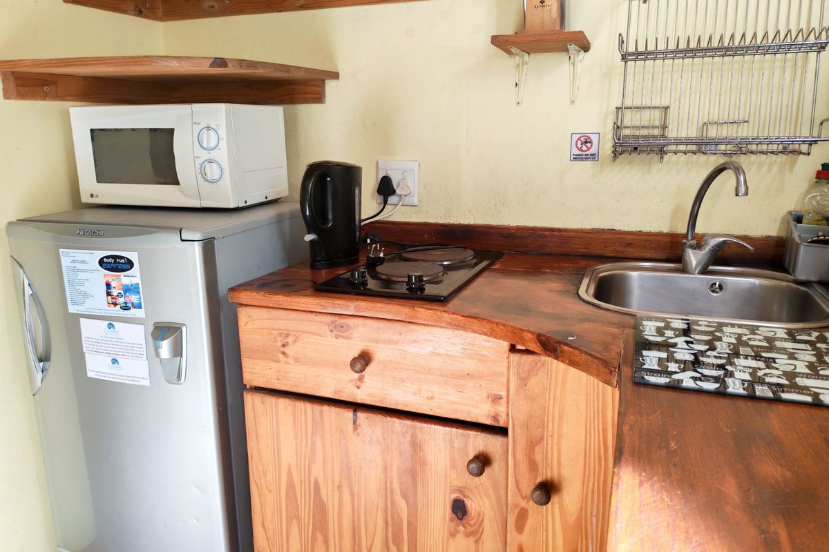 Compact kitchenette featuring wooden cabinetry, a built-in electric hob, stainless steel sink, and wall-mounted storage shelving.