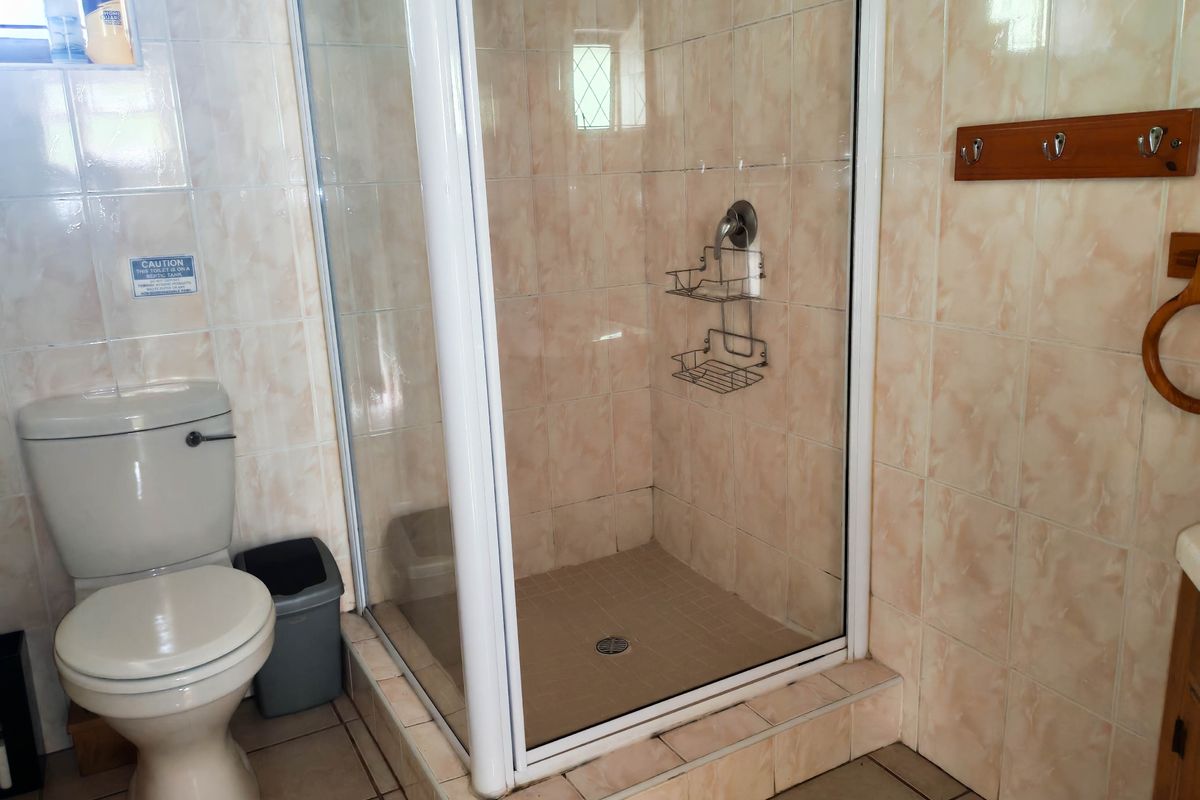 A functional bathroom featuring a glass-enclosed shower, standard toilet, and neutral ceramic wall and floor tiling.
