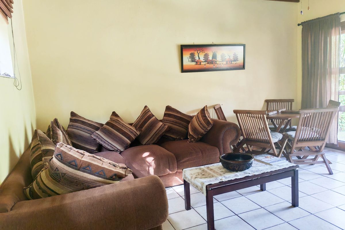 A living room featuring ceramic floor tiles, exposed timber ceiling beams, and a sliding glass door providing access to the exterior.