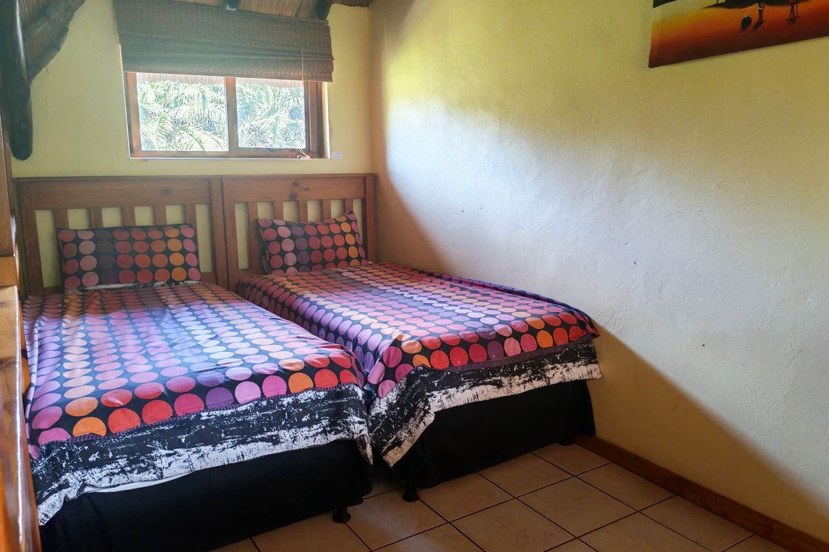 A bedroom featuring tiled flooring, a thatched roof ceiling, and a timber-framed window, showing signs of wear on the wall surfaces.