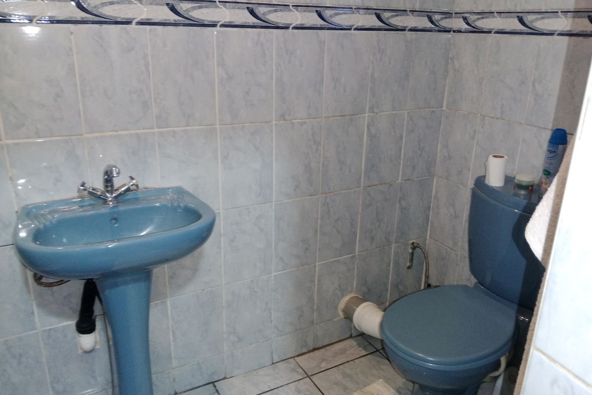 A compact bathroom featuring dated blue sanitaryware, including a pedestal basin and toilet, finished with light blue wall tiles and a decorative border.