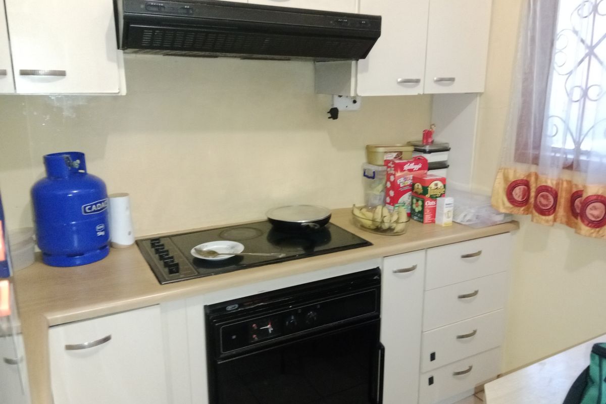 A functional kitchen featuring fitted white cabinetry, laminate countertops, a built-in oven, and an electric hob with an overhead extractor fan.