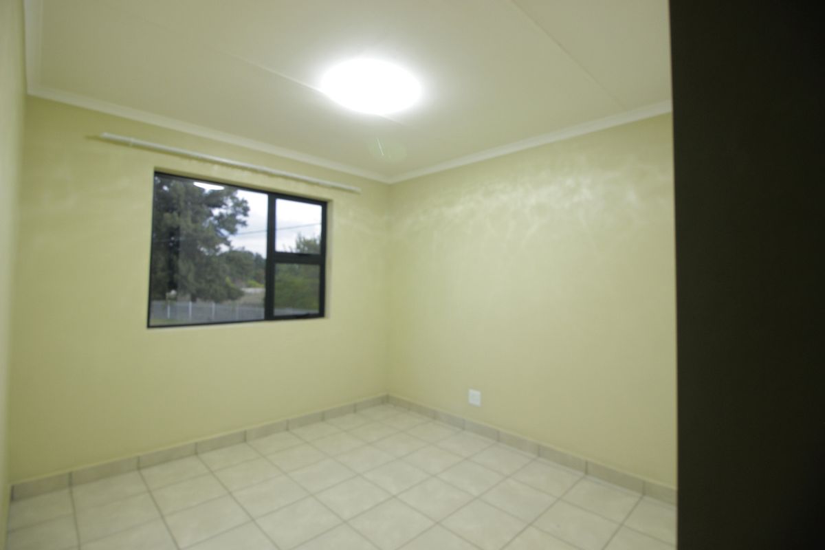 An empty bedroom featuring tiled flooring, neutral wall paint, and an aluminium window frame with a curtain rail.