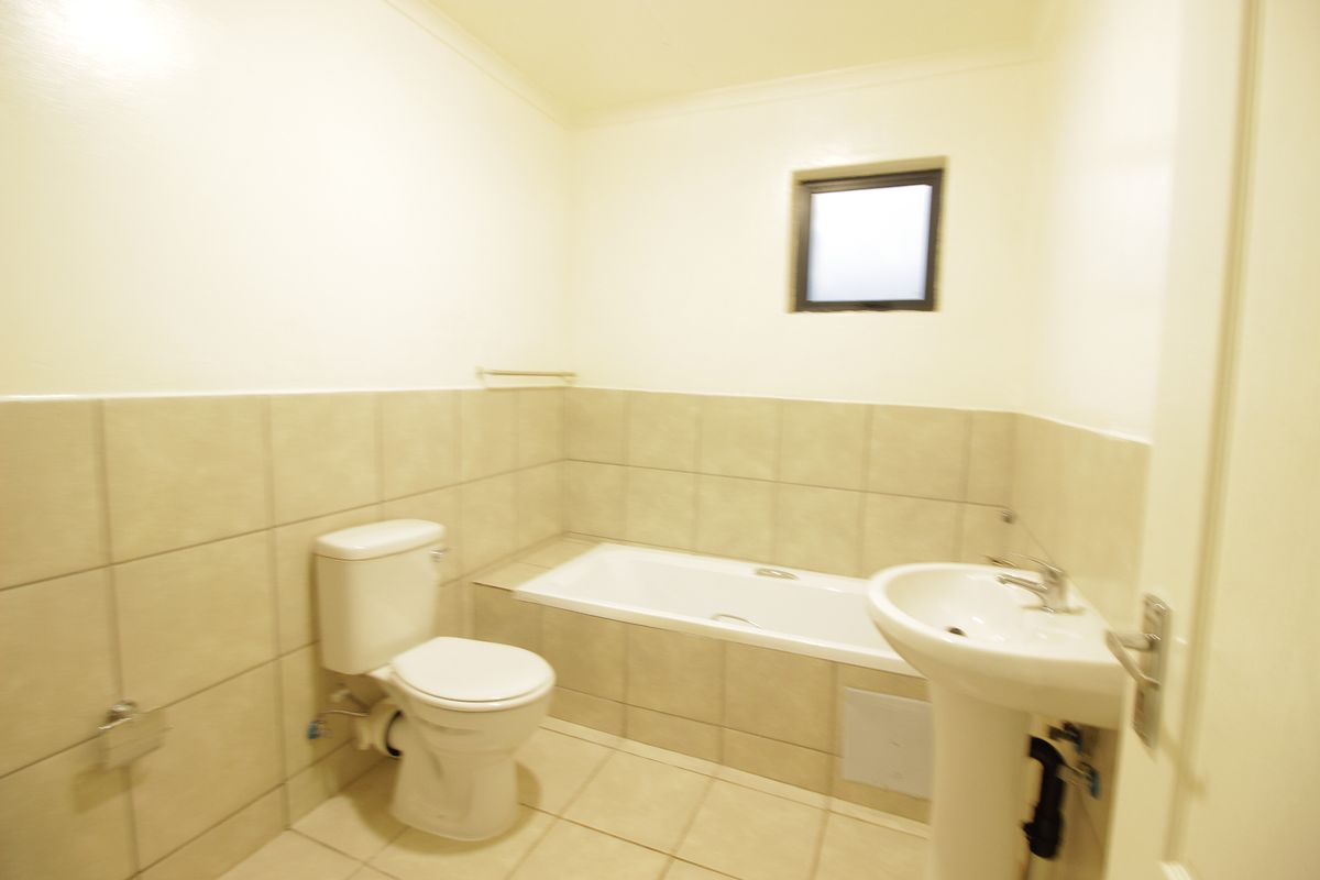 A functional bathroom featuring a pedestal basin, toilet, and a built-in bathtub with neutral wall and floor tiling.