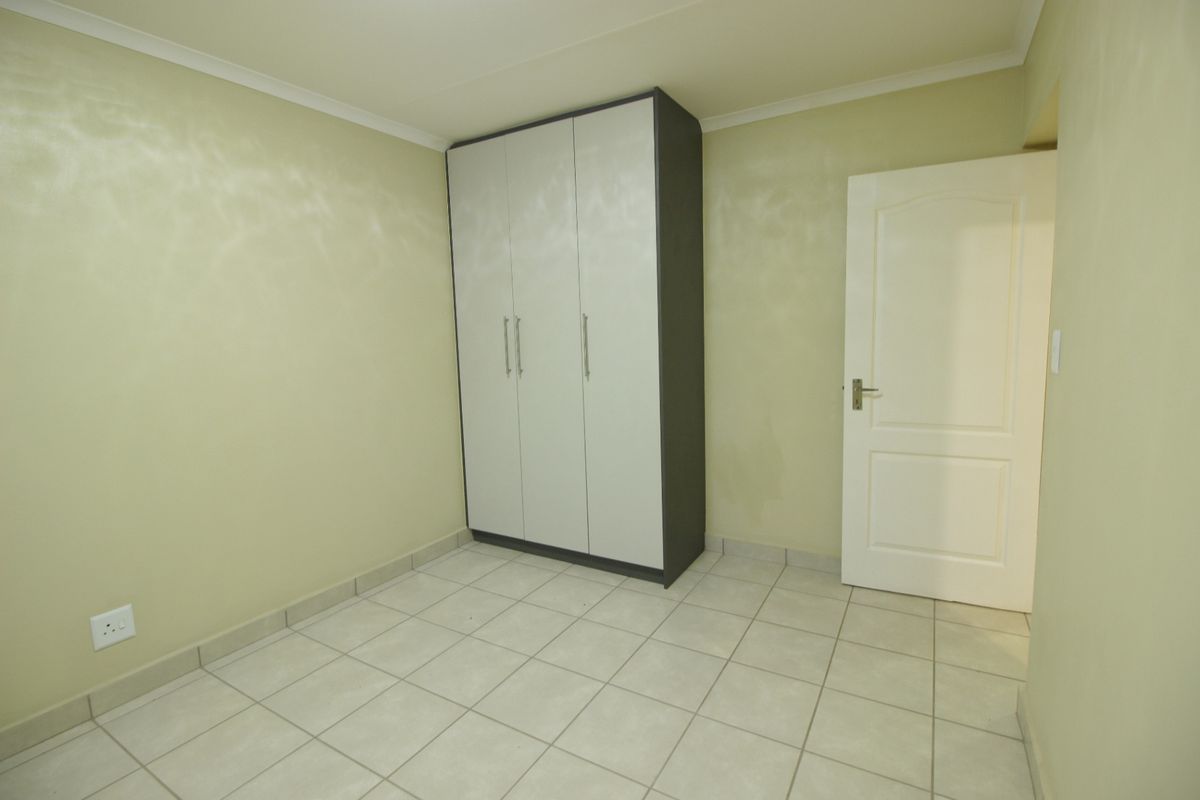 A clean, empty bedroom featuring neutral tiled flooring, coving, and a modern built-in wardrobe with light-colored doors.