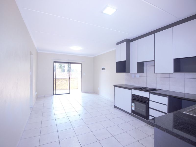 An open-plan kitchen and living area featuring modern cabinetry, built-in appliances, tiled flooring, and a sliding door leading to an outdoor space.