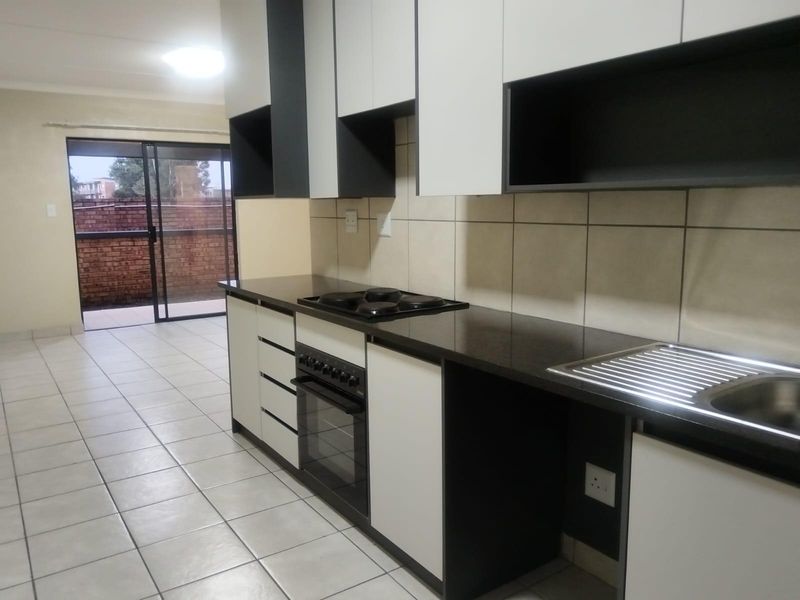 Modern kitchen featuring built-in cabinetry, electric hob, oven, and tiled finishes, leading directly to an outdoor patio area.