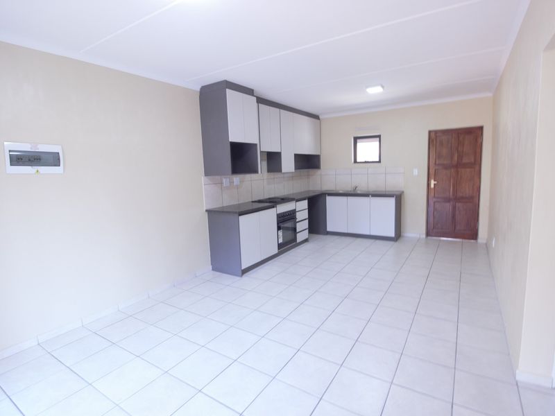 A clean, empty kitchen featuring modern two-tone cabinetry, tiled flooring, a built-in oven and hob, and a tiled backsplash.