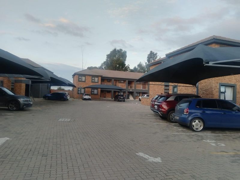 Exterior view of a townhouse complex featuring facebrick buildings, paved parking areas, and installed shade cloth carports for residents.