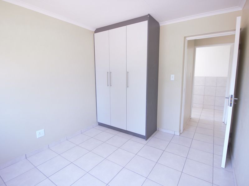 A clean, empty bedroom featuring neutral tiled flooring, a modern built-in wardrobe, and access to an adjacent tiled space.