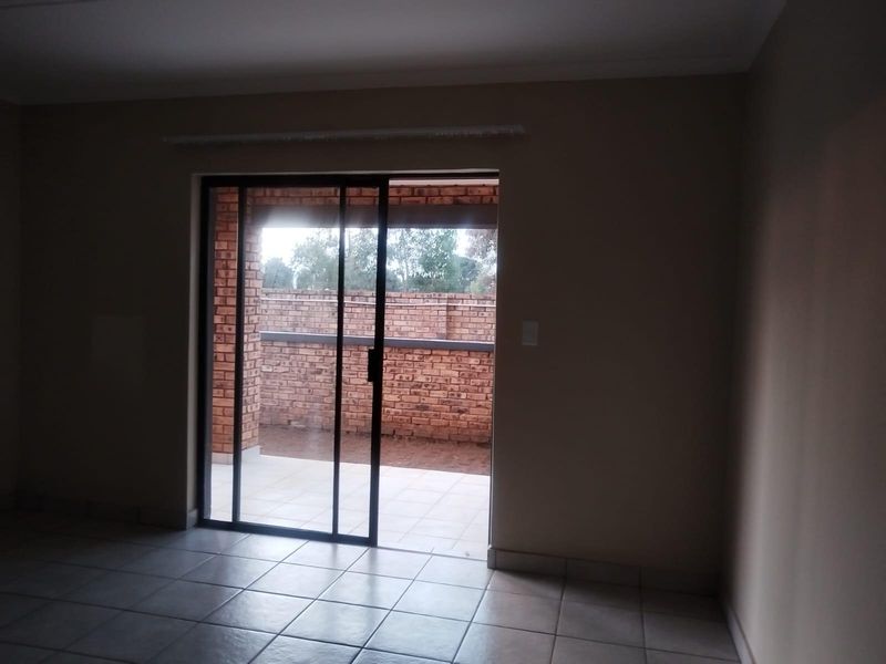 An empty living area featuring neutral tiled flooring and a sliding glass door providing direct access to an outdoor patio space.