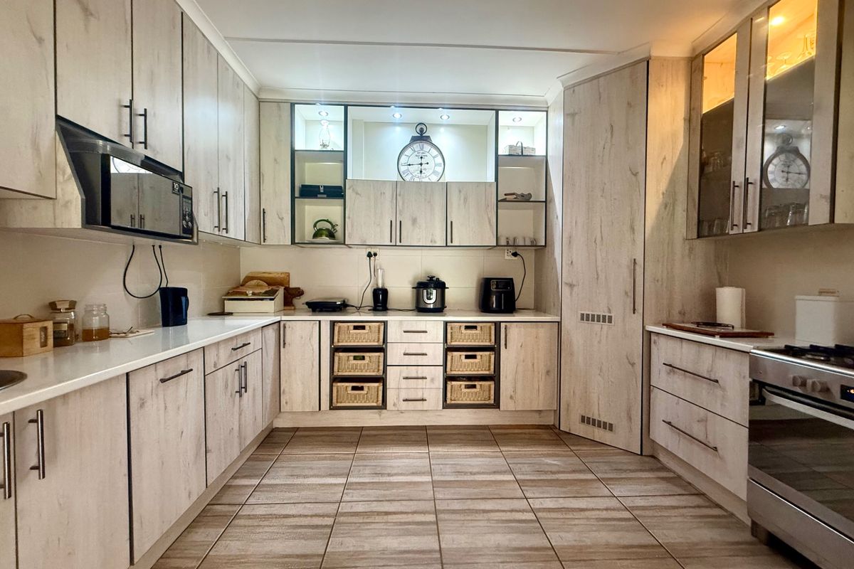 A well-maintained kitchen featuring light wood-grain cabinetry, tiled flooring, integrated lighting, and built-in appliances, offering a clean and functional workspace.