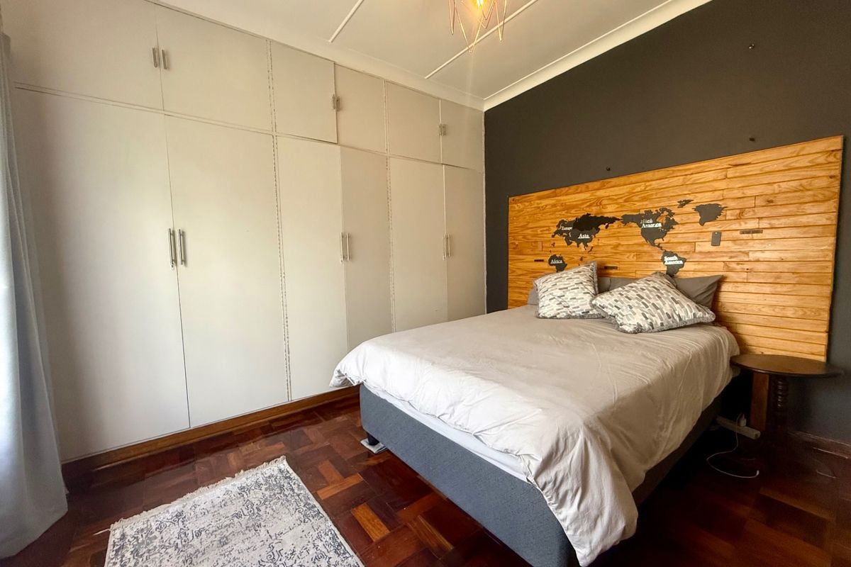 A well-maintained bedroom featuring classic parquet flooring, extensive floor-to-ceiling built-in cupboards, and a decorative wooden feature wall.
