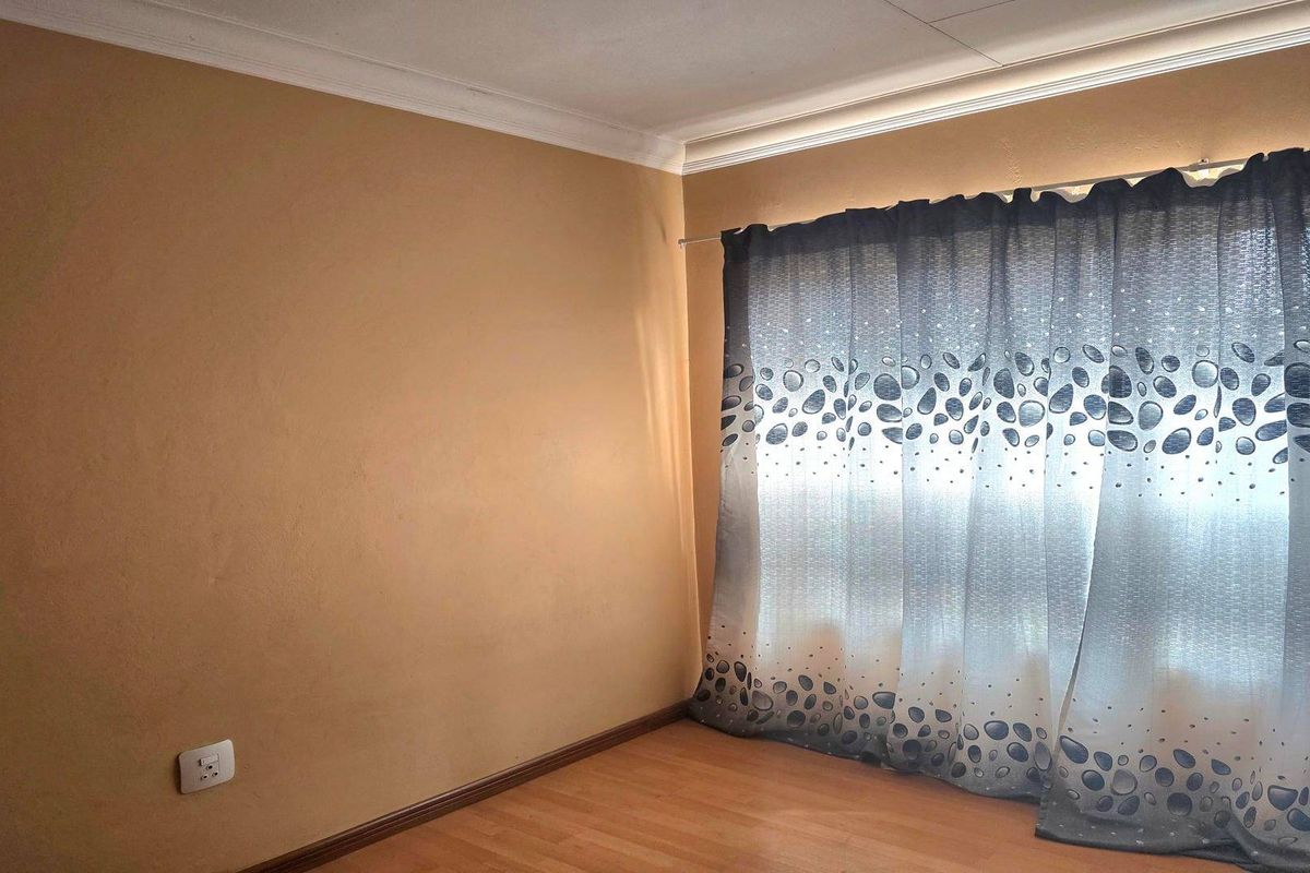 A vacant bedroom featuring laminate flooring, coved ceilings, and a large window covered by patterned curtains.