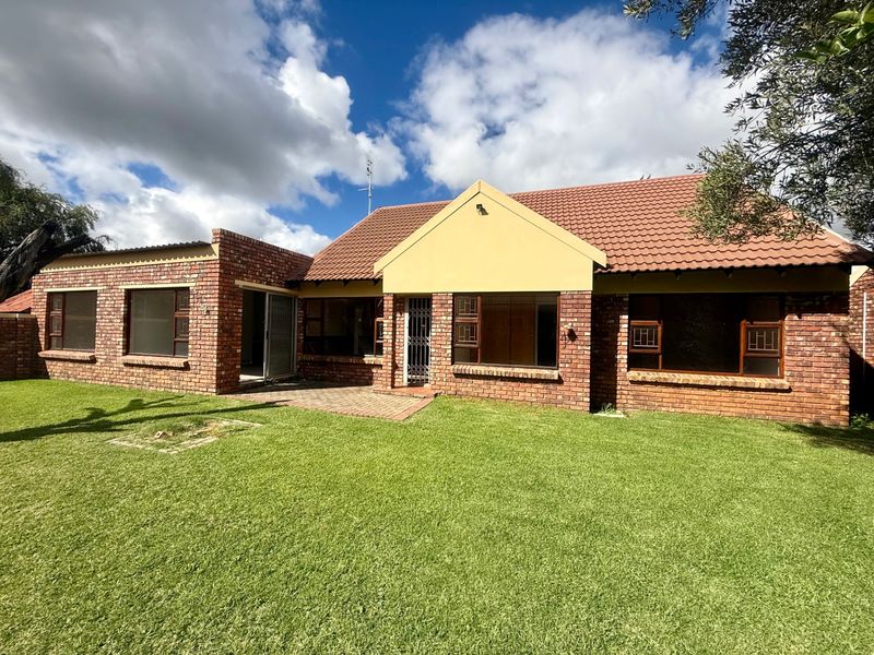 Rear view of a face brick townhouse featuring a tiled roof, paved patio area, and established lawn.