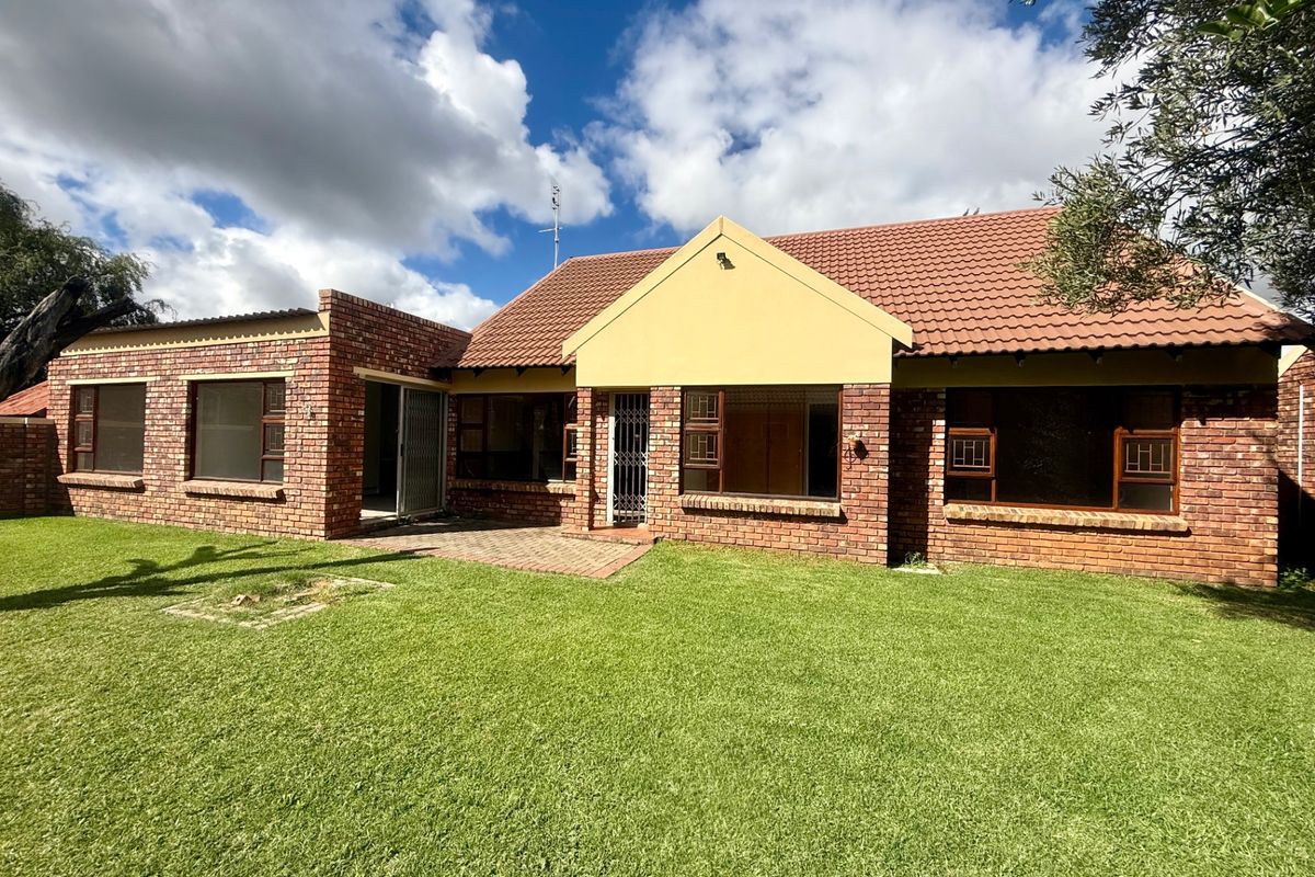 Rear view of a face brick townhouse featuring a tiled roof, paved patio area, and established lawn.