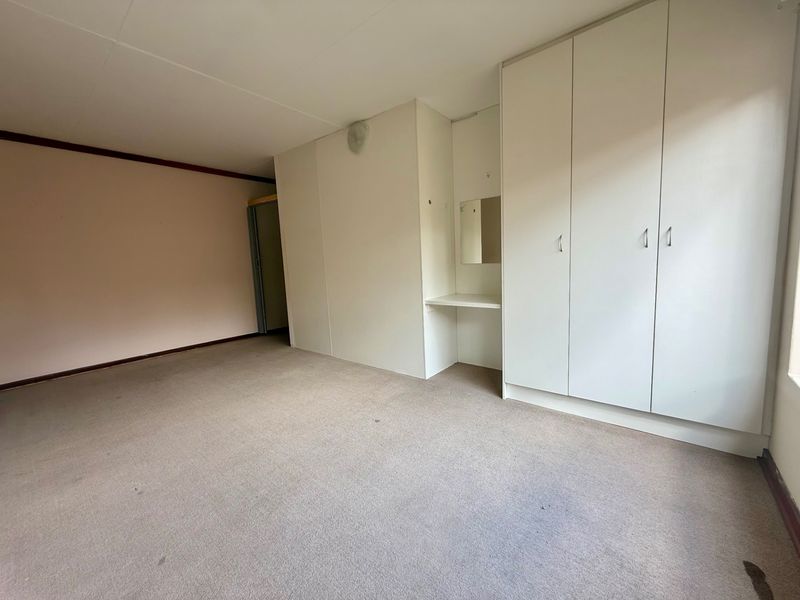 A vacant bedroom featuring built-in cupboards with an integrated vanity nook and carpeted flooring.