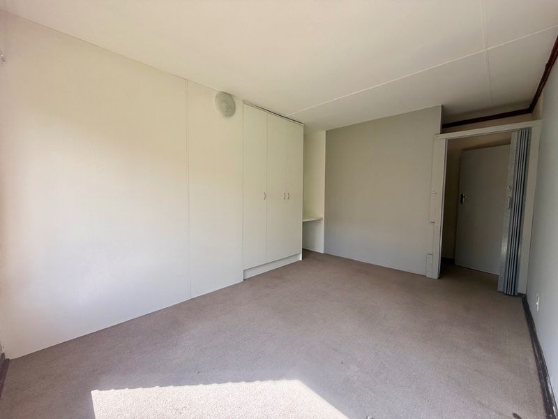 An empty bedroom featuring built-in cupboards, carpeted flooring, and a folding door, offering a blank canvas for personalization.