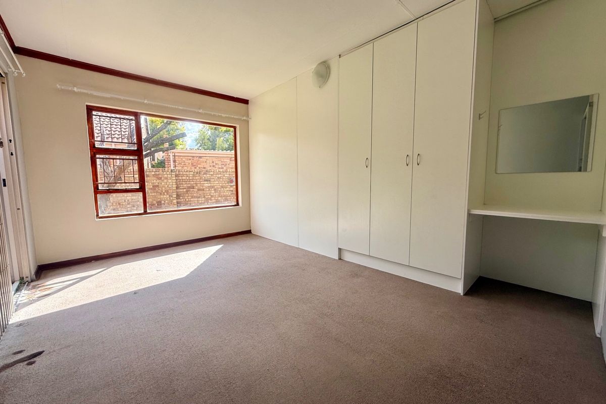 A spacious, empty bedroom featuring built-in cupboards, a vanity area, and large windows, offering a blank canvas for personalization.