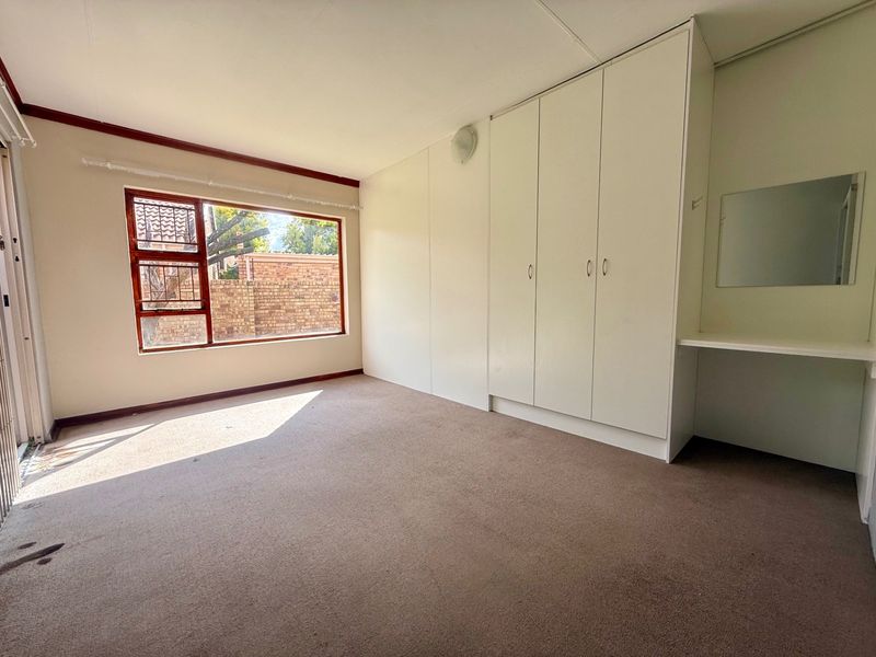 A spacious, empty bedroom featuring built-in cupboards, a vanity area, and large windows, offering a blank canvas for personalization.