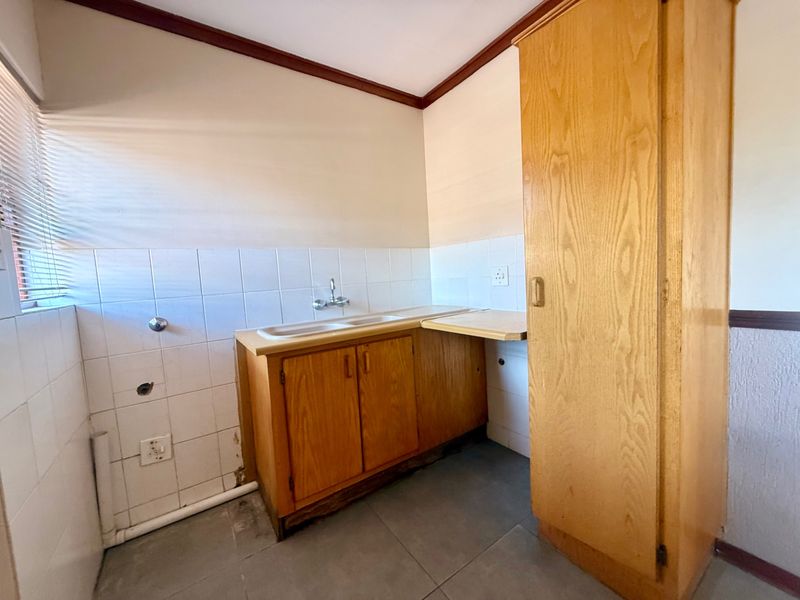 A functional laundry area featuring built-in wooden cabinetry, a double sink, and tiled splashbacks, requiring some maintenance and cosmetic updates.